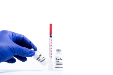 Doktor beyaz arka planda mavi eldivenli aşı şişesini tutuyor. Yanında aşı şişesi olan bir şırınga.