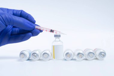 Doktorun elinde mavi eldivenli beyaz arka planda aşı şişesi olan bir şırınga var. tıbbi konsept