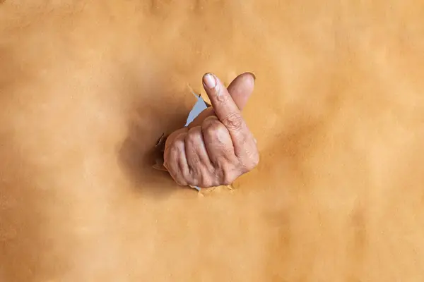 Stock image Indian woman hand showing symbol korean mini heart gesture through the torn holes of brown paper background with space for text.