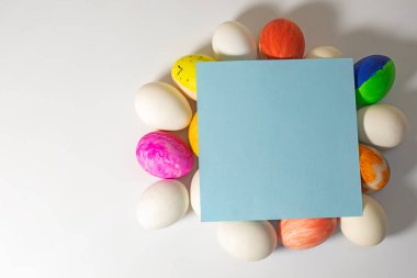 Renkli paskalya yumurtaları ve beyaz zemin üzerinde mavi kart ve metin için boşluk