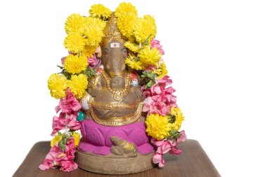 Ganesha Chaturthi festivali için evde çiçek çelenkleriyle süslenmiş ahşap masadaki Hindu tanrı Ganesha putu..
