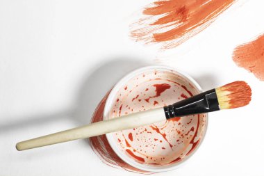 Boya kutusunun üstünde boya fırçası ve beyaz arka planda kırmızı boya. Üst görünüm