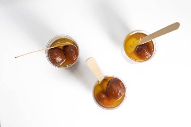 Top view of delicious Gulab Jamun sweets served in cups filled with syrup with wooden spoons on white background. clipart