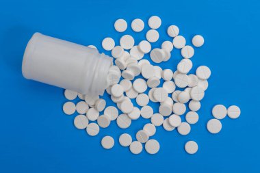 Beyaz tabletlerin yakın plan görüntüsü bir şişeden parlak mavi bir yüzeye saçılmış..