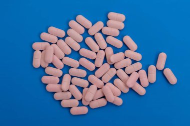 Mavi bir yüzeye saçılmış pembe hapların yakın plan görüntüsü, sağlık sigortası kavramı..