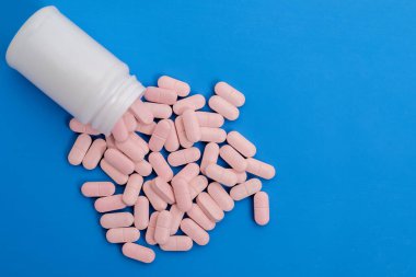 Pembe haplar beyaz bir plastik ilaç şişesinden temiz bir mavi arka plana döküldü. Tıbbi ve sağlıkla ilgili görseller için mükemmel..