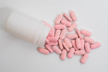 Pembe haplar beyaz plastik bir ilaç şişesinden temiz beyaz bir arka plana döküldü. Tıbbi ve sağlıkla ilgili görseller için mükemmel..
