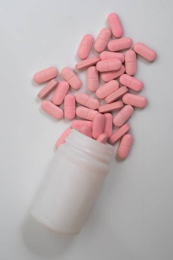 Pembe haplar beyaz plastik bir ilaç şişesinden temiz beyaz bir arka plana döküldü. Tıbbi ve sağlıkla ilgili görseller için mükemmel..