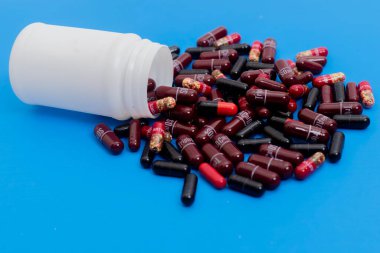 Parlak mavi arka plan, sağlık, ilaç ve eczane kavramlarına saçılmış kırmızı ve siyah ilaç kapsüllü beyaz plastik bir şişe..