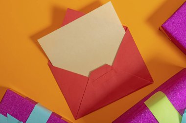 Turuncu bir arkaplana yerleştirilmiş içi boş bir mektup içeren renkli bir zarf. Etrafı parlak paketlenmiş hediye kutularıyla çevrili..