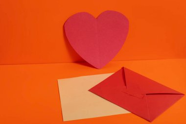 Parlak turuncu bir zemin üzerinde zarflarla süslenmiş kırmızı bir kalp. Sevgililer Günü, düğünler ya da içten mesajlar gibi konular için mükemmel..