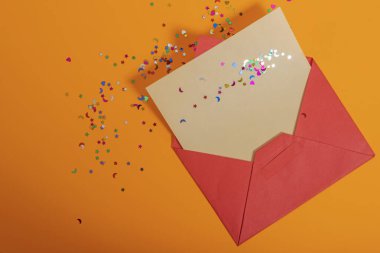 Renkli konfeti içeren kırmızı bir zarf turuncu bir arka plana doğru canlı bir şekilde yayılıyor..