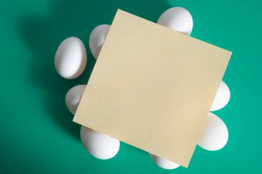 Happy Easter. A blank sheet of paper placed on top of a white egg placed on a vibrant green background. clipart