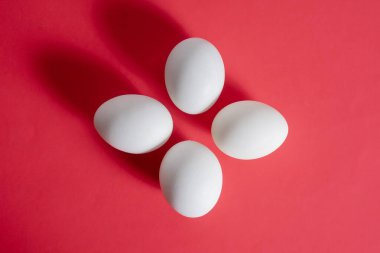 Four white eggs are beautifully arranged in a symmetrical pattern on a bold red background. clipart