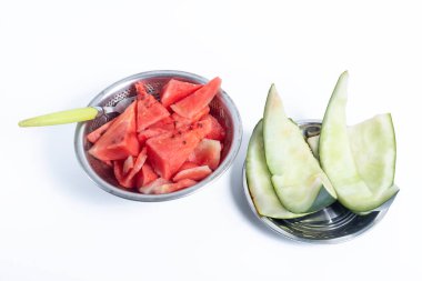 A close-up of cut watermelon ready to eat with spoons in metal bowls on a white background, with discarded watermelon rinds on a metal grate next to it, showing freshness and simplicity. clipart