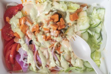 Domates, marul, salatalık ve kremalı sos gibi taze sebzelerle dolu canlı bir salatanın en üst görüntüsü..