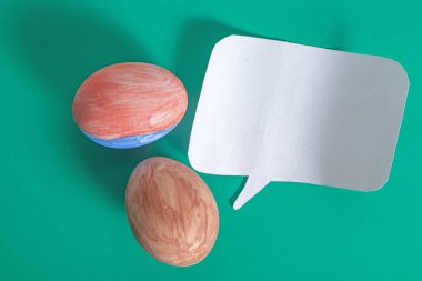 Canlı yeşil bir yüzeye yerleştirilmiş renkli bir yumurta ve kağıt konuşma balonu, iletişim ve şenlikli dekorasyonlar..