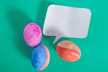 Canlı renkli Paskalya yumurtaları ve mesaj veya mesaj için yeşil zemin üzerinde boş kağıt konuşma balonu.