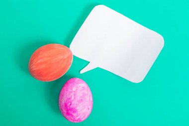 Parlak renkli Paskalya yumurtaları, boş bir kağıt konuşma baloncuğuyla donuk arka planda mevsimlik tasarımlar için mükemmel..