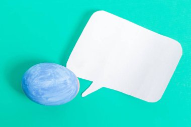 Canlı bir turkuaz yüzeyde beyaz bir konuşma balonunun yanına yerleştirilmiş mavi bir yumurta iletişim ve Paskalya kutlaması temalarını temsil eder..