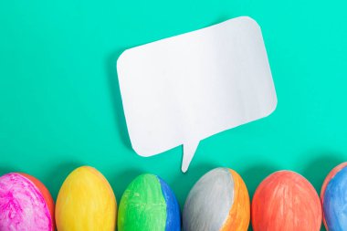 Canlı bir Paskalya yumurtası görüntüsü parlak mavi arka planda düz beyaz bir konuşma baloncuğuyla hizalanmış. Yaratıcı iletişim, Paskalya kutlamaları ya da şenlikli tasarımlar için mükemmel..