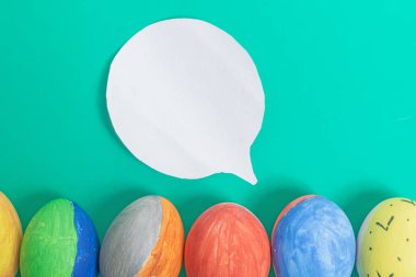 Parlak yeşil bir yüzey üzerinde boyanmış Paskalya yumurtalarının canlı bir düzeni, üzerinde beyaz bir konuşma balonu var..