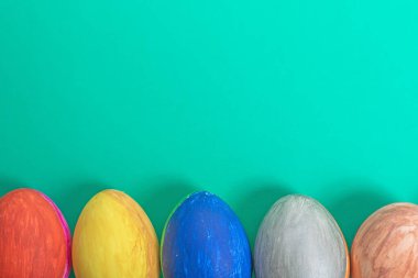 Neşeyi ve kutlamayı sembolize eden çeşitli parlak Paskalya yumurtaları canlı yeşil bir arka plana yerleştirilir..