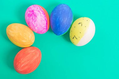 Saf yeşil bir yüzeyde resmedilen parlak renkli ve dekore edilmiş Paskalya yumurtaları, neşeli bir atmosfer ve tatil neşesi uyandırıyor..