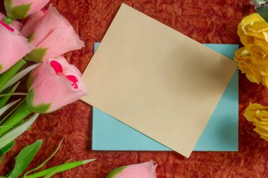 Renkli kumaş desenli bir kumaş üzerinde canlı dekoratif çiçeklerle dolu boş bir kart. Tebrik kartı tasarımları ve kutlama temaları için harika.