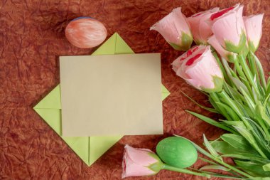 Pembe çiçekler, boş bir kart ve Paskalya temalı dekorasyonların yer aldığı, mevsimsel selamlama ve yaratıcı davet için mükemmel bir apartman dairesi..