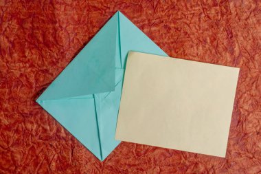 Boş bir kağıt parçası ve kırmızı arkaplana yerleştirilmiş mavi bir zarf. Kırtasiye malzemeleri, davetiyeler, mektuplar, yaratıcı projeler için mükemmel..