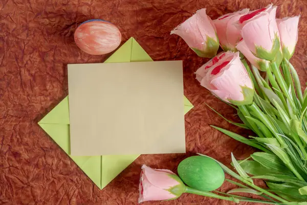 Pembe çiçekler, boş bir kart ve Paskalya temalı dekorasyonların yer aldığı, mevsimsel selamlama ve yaratıcı davet için mükemmel bir apartman dairesi..