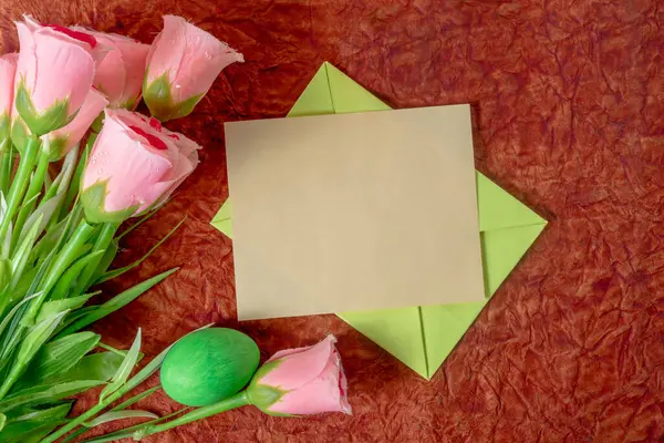 Yeşil bir zarfın içinde yeşil güller ve kırmızı bir yüzeye yerleştirilmiş yeşil bir Paskalya yumurtasıyla çevrili boş bir kart. Paskalya, tebrik kartları ya da Sevgililer Günü temaları için mükemmel.