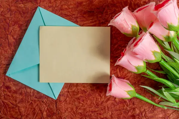 Pembe güller zengin bir yüzeye yerleştirilir. Boş bir kart ve zarfın yanına. Aşk, romantizm ve kalpten bir bağın temalarını çağrıştırır..