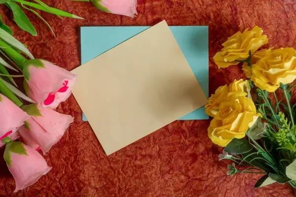 Pembe ve sarı çiçeklerle çevrili desenli bir yüzeye yerleştirilmiş boş bir kart çeşitli durumlar için neşeli ve davetkar bir ışık sağlar..