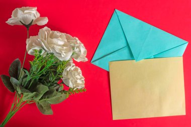 Parlak kırmızı bir yüzey üzerinde canlı yeşil yapraklarla süslenmiş zarif beyaz çiçekler kutlama, romantizm ya da içten bir iletişim için mükemmeldir..