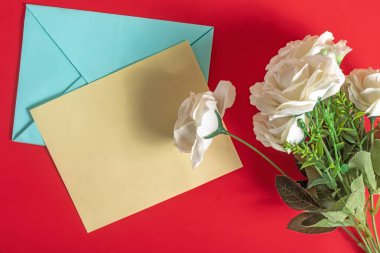 Bir kağıt kart, zarf ve beyaz güller göz alıcı kırmızı bir yüzey üzerinde, kutlama, romantik mesajlar veya düşünceli yazışmalar için mükemmel bir düzenleme.