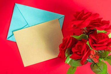 Kırmızı yüzeyinde sarı bir tebrik kartı olan parlak kırmızı güller, sevgi ve sevgiyi ifade eder..