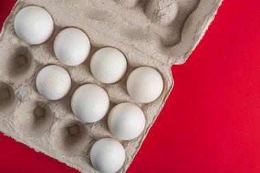 Koyu kırmızı arka planda taze beyaz yumurtalar tutan açık bir karton yumurta kutusu. Temiz ve minimal bir kompozisyon.