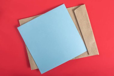Mavi kağıt ve kahverengi zarf güzel bir şekilde canlı kırmızı bir yüzeye yerleştirilmiş, minimalist bir tasarım sergiliyor..