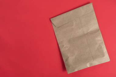 Çevre dostu fikirleri ve minimalizmi sembolize eden canlı kırmızı bir arka plana yerleştirilmiş kahverengi bir kese kağıdı..