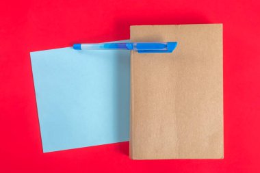 Düz kompozisyonda bir defter, mavi bir sayfa kağıt ve kırmızı zemin üzerinde bir kalem vardı. Yazarlık, eğitim ve yaratıcılık konuları için mükemmel.