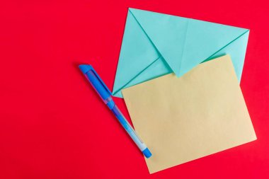Mavi bir zarf, sarı bir kağıt parçası ve kırmızı arka plana ustalıkla yerleştirilmiş mavi bir kalem. İletişim, yazım ve yaratıcılıkla ilgili kavramlar için uygundur.