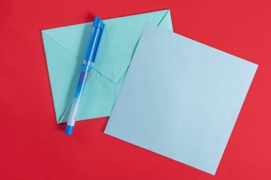Mavi bir kalem ve uyumlu mavi bir kağıt zarf canlı kırmızı bir yüzeye yerleştirilir, yaratıcılık ve iletişimi ifade eder..