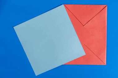 Parlak mavi arkaplan üzerinde boş mavi kağıt olan kırmızı zarfın üst görünümü.