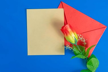 Kırmızı bir zarf ve mavi arka planda süs çiçeği olan boş bir kart. Sevgililer Günü, yazışmalar ve kutlama temaları için mükemmel..