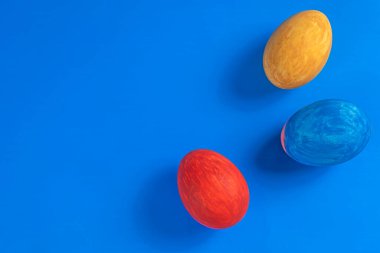Kırmızı, sarı ve mavi renkli üç Paskalya yumurtası, kutlama ve mevsimsel projeler için harika bir minimalist tasarım olan parlak mavi arka plana karşı dizayn edilir..