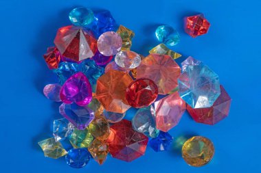 Değişik kesikler ve parlak renkler gösteren parlak mavi bir yüzeye yerleştirilmiş renkli şeffaf plastik taşlar..