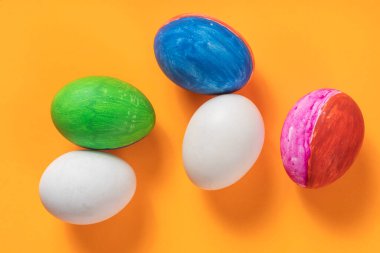 Turuncu bir yüzey üzerinde dinlenen canlı Paskalya yumurtalarının üst görüntüsü sanatsal renkli desenler sergiliyor..