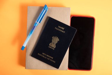 Hindistan pasaportu, seyahat ve belgelerin esaslarını sembolize eden parlak sarı bir yüzeye defter, kalem ve akıllı telefon yerleştirildi..